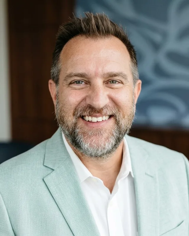 Timothy Hawkins, smiling, in a light green blazer and white collared shirt.